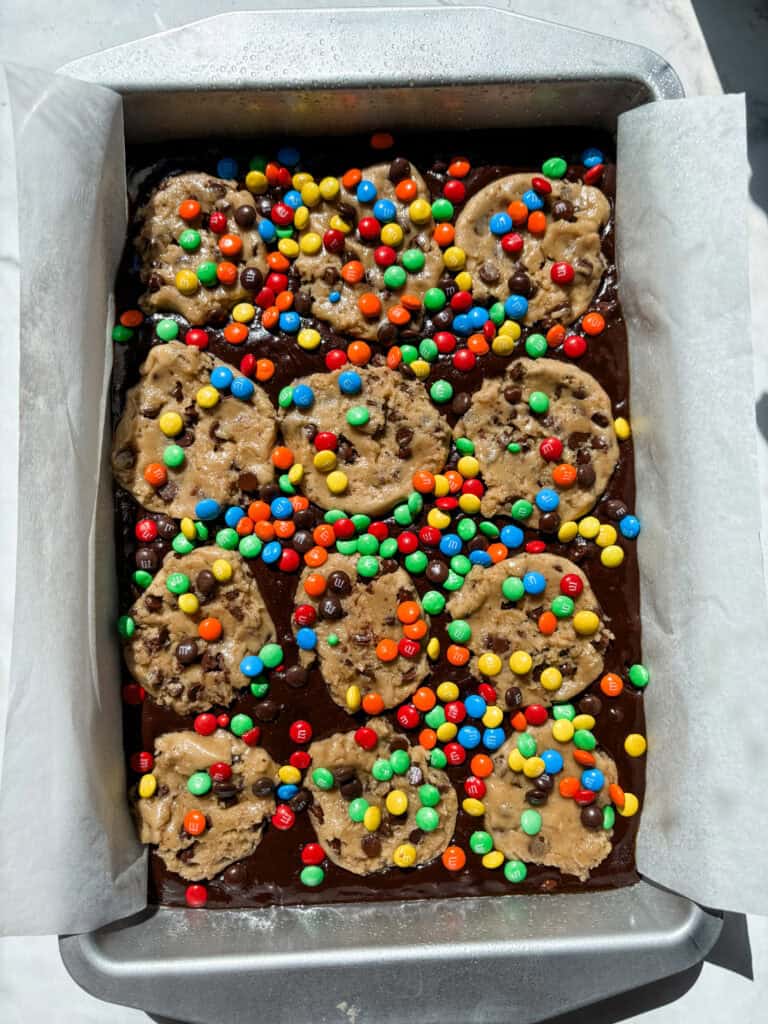 brownie topped with cookie dough and m&m's before being baked